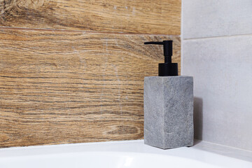 A gray soap dispenser sits on the bathtub. Minimalist modern bathroom interior design.