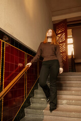 A young beautiful woman stands on the stairs in the entrance of an old house