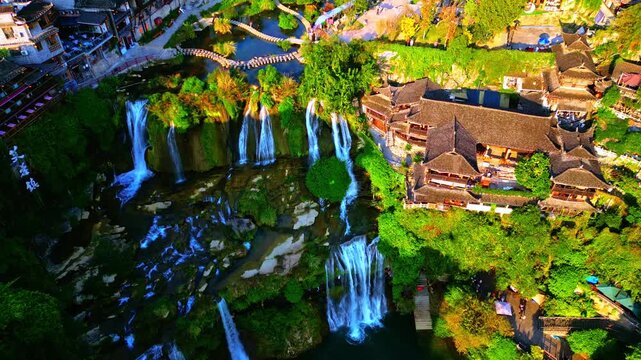 Aerial view of the cascading waterfalls of Furong Ancient Town, contrasting beautifully against the verdant greenery and traditional architecture, China.