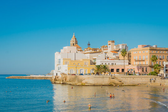 Paisaje costero de Sitges, en Catalu&ntilde;a, Espa&ntilde;a, mostrando las elegantes fachadas de estilo mediterr&aacute;neo frente al paseo mar&iacute;timo, con la iglesia y el casco antiguo al fondo.