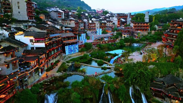 Aerial view of traditional buildings and water features, with lush greenery adding a vibrant contrast, Xiangxi Tujia and Miao Autonomous Prefecture, China.
