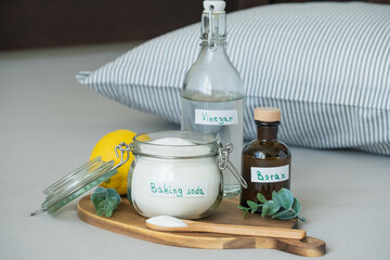 Baking soda, vinegar, lemon and borax, salt are placed on a wooden tray. Sustainable, non-toxic home care solution for fresh and hygienic bedding.