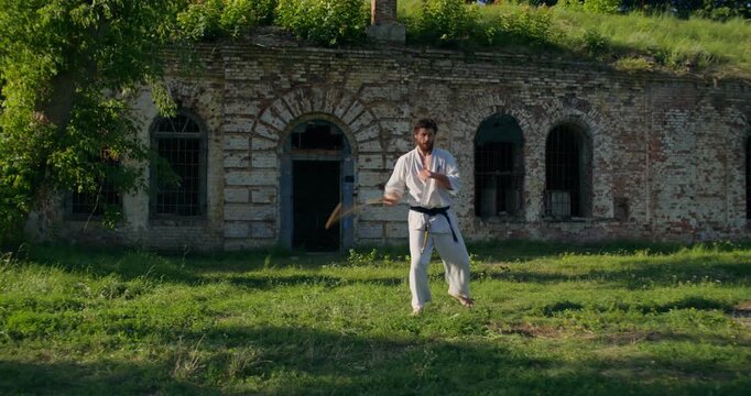 Young man using nunchaku in karate. Two male karate practitioners train on the grass.