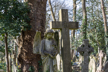 Weathered Stone Angel Statue and Cross in Historic Cemetery, London, UK