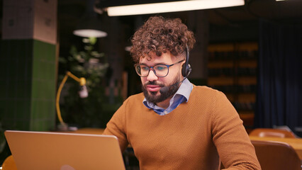Professional middle eastern businessman, contact center operator in headset talking, using laptop