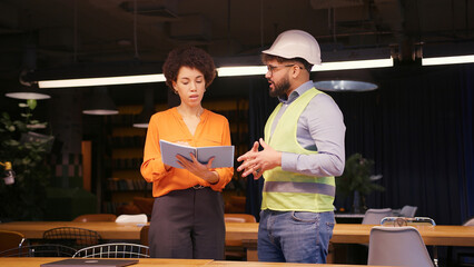Male project manager discussing building plan with female engineer in hard hat and safety vest