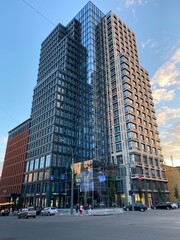 Modern high-rise residential building in an urban city environment during daylight. Contemporary architecture with glass facade and geometric design, surrounded by streets and pedestrians. © eeesttc