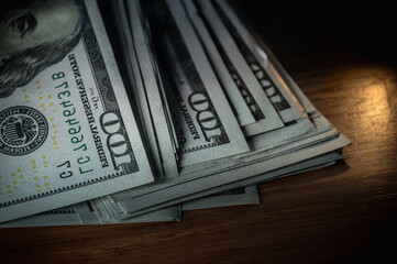 A pile of paper money: American dollars in denominations of $100 and $100 bills. A stack of crumpled bills on a wooden oak table, close-up, blurred, with selective focus. banner copy space