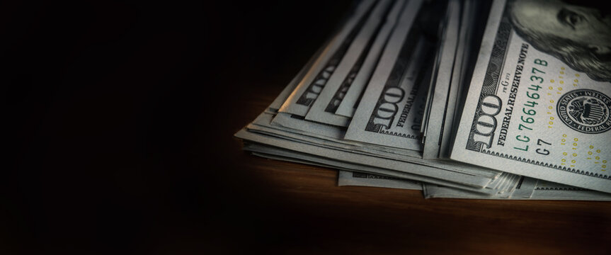 A pile of paper money: American dollars in denominations of $100 and $100 bills. A stack of crumpled bills on a wooden oak table, close-up, blurred, with selective focus. banner copy space