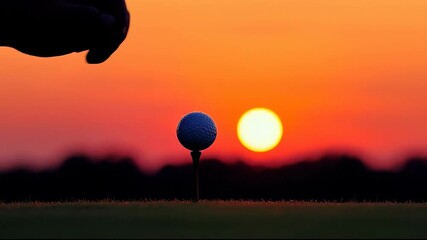A hand placing a golf ball on a tee at sunset.