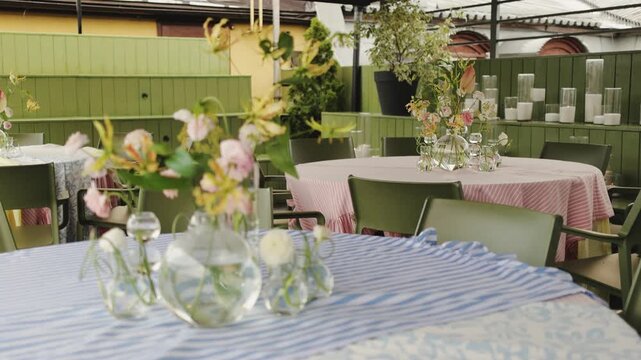 glass vases and loose blooms on striped tablecloth with pink linen in background, venue setup for rehearsal