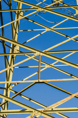Abstract geometric pattern of a yellow steel power line pylon against a clear blue sky