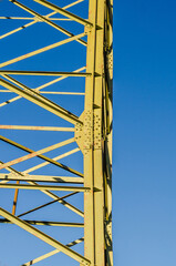 Close-up view of a yellow steel lattice tower against a clear blue sky