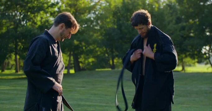 Two male karate practitioners preparing for training and putting on black keikogi. The karate practitioners put on black keikogi and prepare to train.