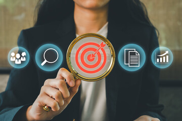 Businesswoman using magnifying glass with target icon, symbolizing focus on business strategy, goals, and success.