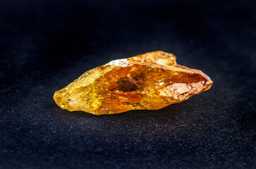 Raw amber resin chunk with translucent golden-orange hues on a dark textured surface