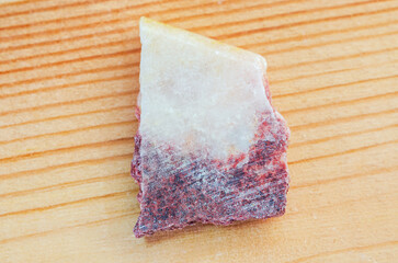 Close-up macro shot of a rough, unpolished mineral specimen with white and red hues on wood