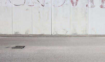 Grunge concrete  wall with an erased old writing in the upper side. Sidewalk and and street in front. Background for copy space.