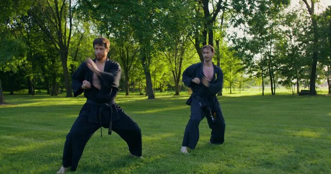 Two karate practitioners combine different striking techniques during training. The karate practitioners put on black keikogi and prepare to train.