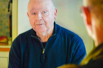Quality mature lifestyle of older man talking to friend indoors, calm attentive expression and everyday social interaction reflecting mindful aging and life balance.