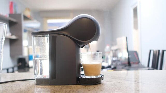 Capsule coffee machine brewing fresh espresso into a glass cup on a kitchen countertop in a modern interior.