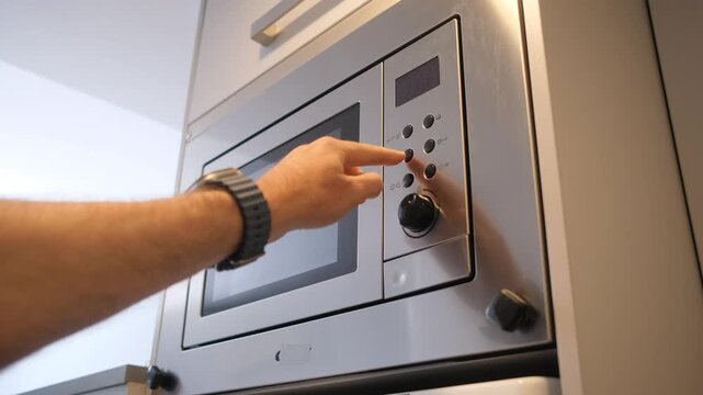Close-up of a hand operating a stainless steel microwave with digital controls for heating food at home.
