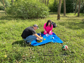 Couple having a casual picnic in a sunny park, cutting a fresh watermelon on a blue blanket.