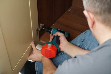 Handyman installing a cabinet door hinge with a cordless power drill during a home improvement project.