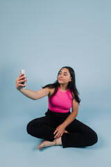 portrait of young latin teenager girl taking a photo selfie and using phone with copy space on blue background in Mexico Latin America, Hispanic brunette woman