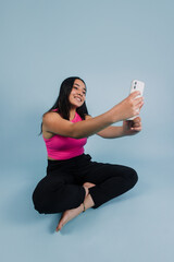portrait of young latin teenager girl taking a photo selfie and using phone with copy space on blue background in Mexico Latin America, Hispanic brunette woman