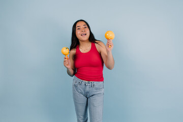 portrait of young latin teenager girl dancing and holding maracas with copy space on blue background in Mexico Latin America, Hispanic brunette woman