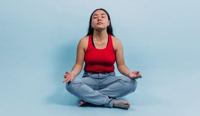 young latina teenager girl doing yoga or meditation with copy space on blue background in Mexico Latin America, Hispanic brunette woman