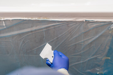 Closeup photo of man holding spatula ready to bathtub repair. Hand in glove holding scraper near masked bathtub edge