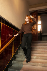 A young beautiful woman stands on the stairs in the entrance of an old house