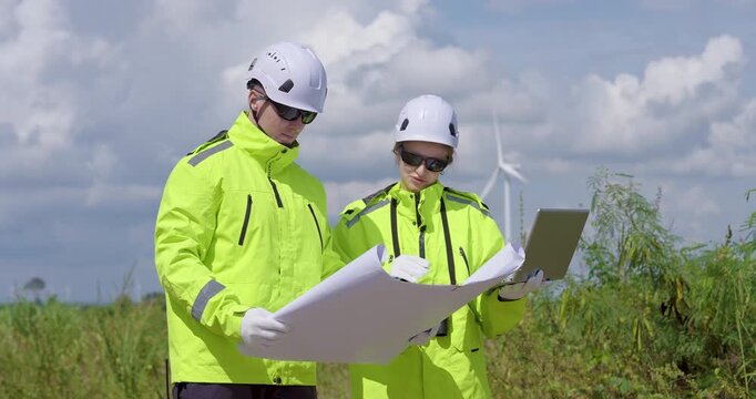 Caucasian engineers review blueprint plan at wind farm check turbine installation progress and structure alignment ensure safety and precision for renewable clean energy technology project
