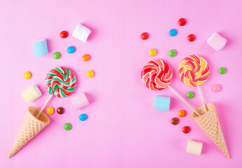 Lollipops, multicolored candies, waffle cones and marshmallows on pink. Colorful flat lay with sweets assortment. Copy space, top view