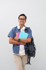 Close up photo of young Asian man wearing casual clothes, backpack, holding book, posing standing confidently while looking at camera with smile, isolated on white background.