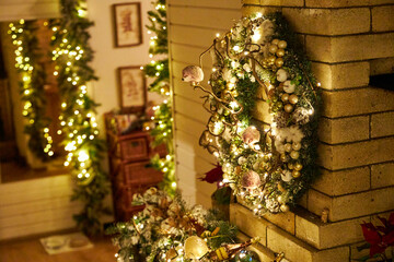 Cozy Christmas interior with festive garland lights and beautifully decorated holiday wreath on a brick fireplace. Warm home atmosphere, holiday spirit, winter celebration and family comfort