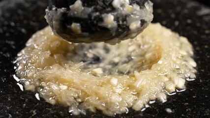Closeup view of a hand expertly grinding fresh garlic cloves with a traditional stone pestle in a dark mortar preparing aromatic ingredients for a delicious meal showcasing authentic culinary techniq.