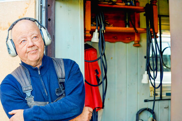 Quiet confidence as an older man wearing hearing protection at a workshop entrance, composed posture and readiness reflecting experience and safety in hands on work.