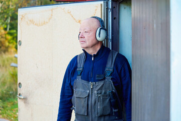 Focused readiness for workshop task with an older man standing at workshop door wearing protective earmuffs, calm attention and professional habit shaped by long experience.