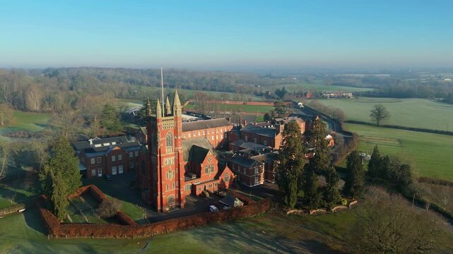 Aerial view of red brick buildings and green fields, with trees and a road winding through the landscape, Rugby, England, United Kingdom.