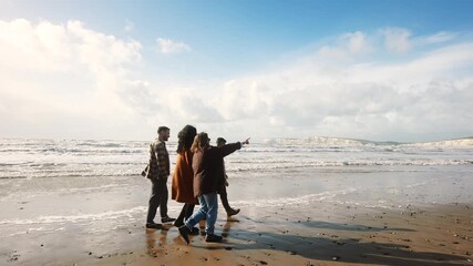A group of people are walking on the beach, enjoying the ocean view. Scene is peaceful and relaxing