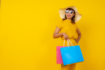 happy young Asian woman in yellow jumpsuit and straw hat jumping for joy on isolated yellow background, summer vacation, fashion travel and energy lifestyle concept.