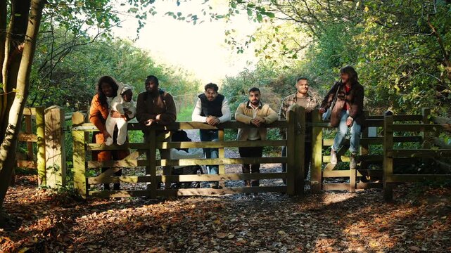 A group of people are standing in front of a wooden fence, posing for a picture. Scene is lighthearted and fun, as the group of people seem to be enjoying their time together
