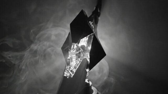 Abstract dark crystal sculpture with multifaceted geometric shapes reflecting light against ethereal smoke, in monochrome