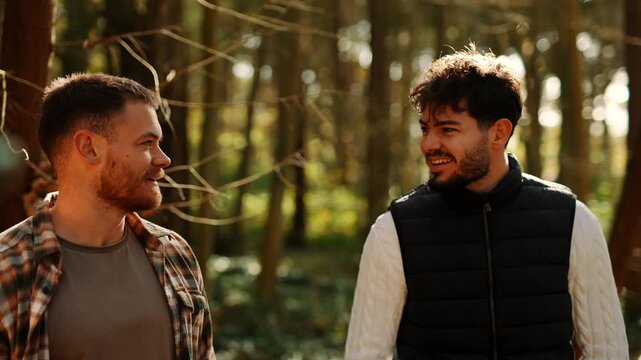 Two men are walking in a forest, one of them is wearing a plaid shirt. Scene is lighthearted and casual