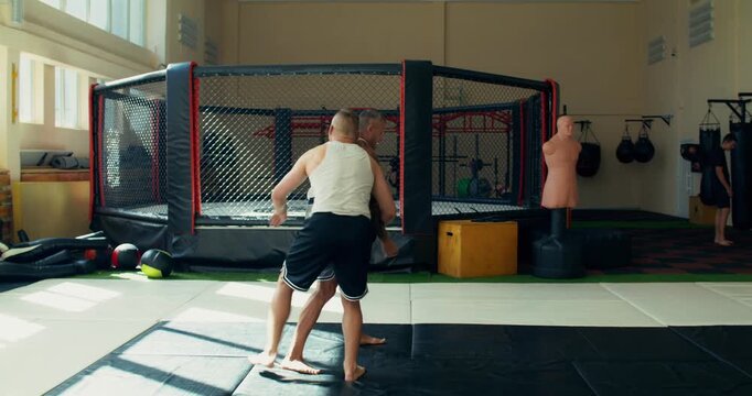 Two male mixed martial artists practice takedowns during training.