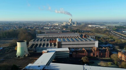 Aerial view of industrial factory buildings with a towering chimney, set against a backdrop of the city, Rugby, England, United Kingdom.