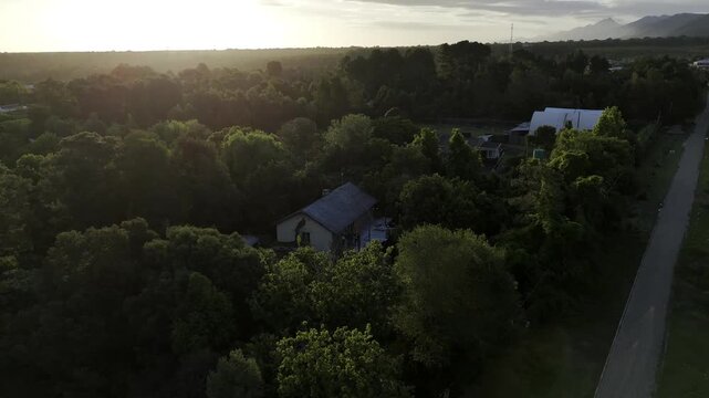 Drone flies up and away from backpacker hostel in a forested community at base of the Tsitsikamma Mountains at sunset in Stormsrivier, Eastern Cape, South Africa